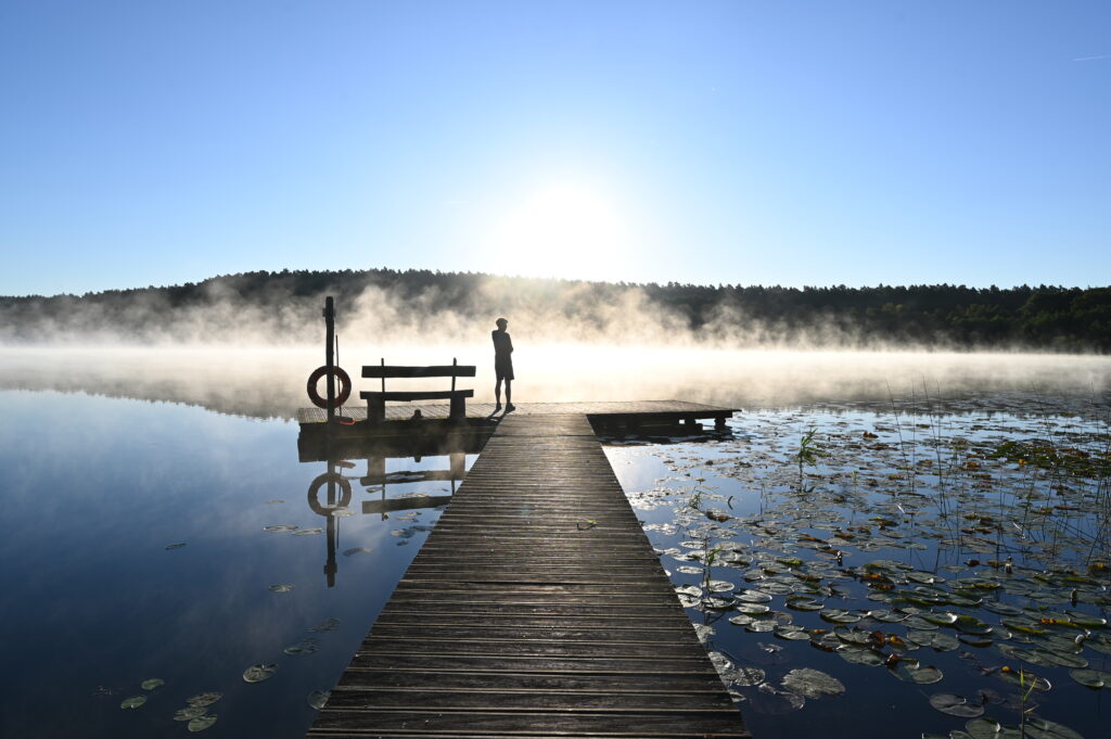 Mann auf angelsteg vor nebel und sonne